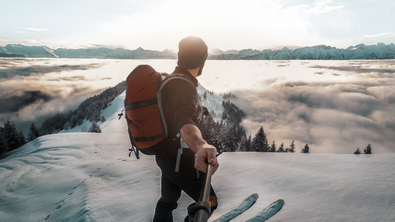 Man holding a selfie stick in the snow on a mountain.