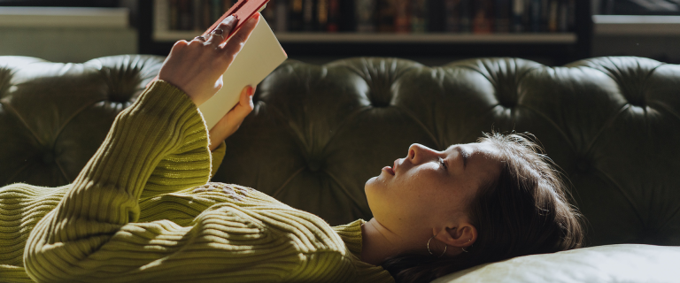 Woman lying on couch reading a book